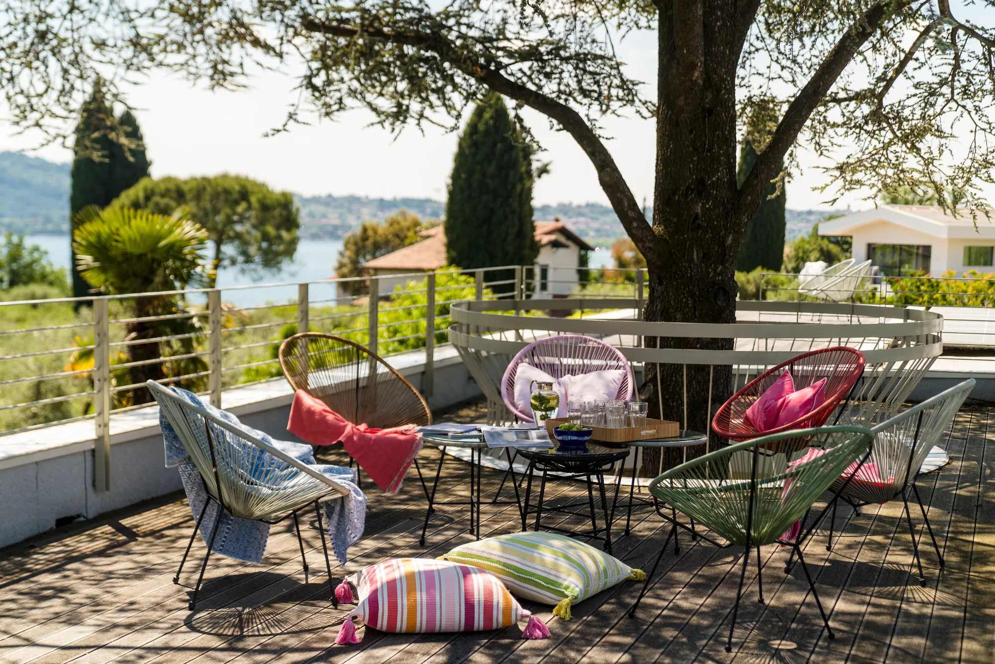 Colorful Acapulco chairs and cushions on the roof terrace under the cedar, Lake Garda behind