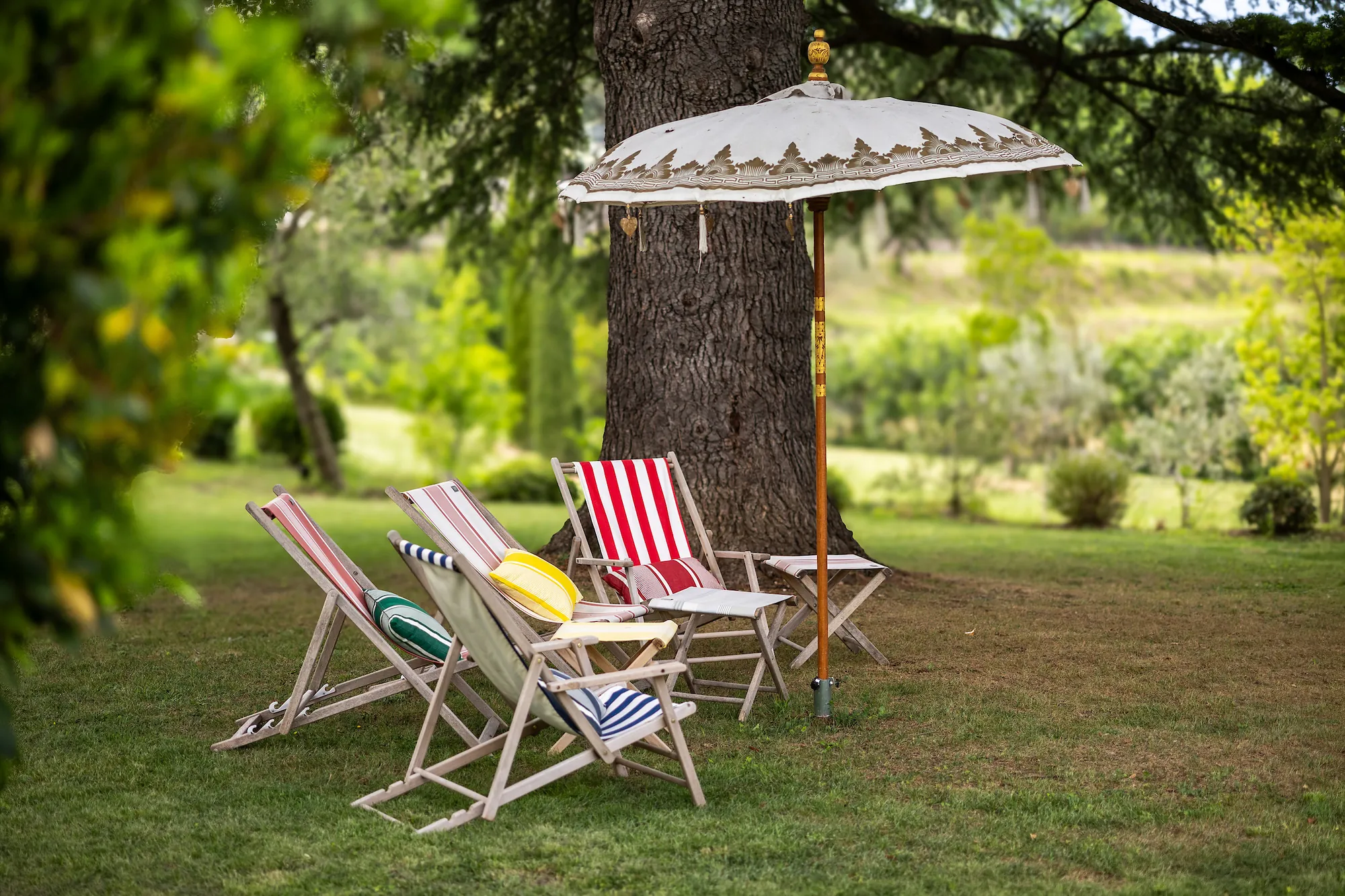 Striped deck chairs and a fringed parasol under the old cedar in the garden