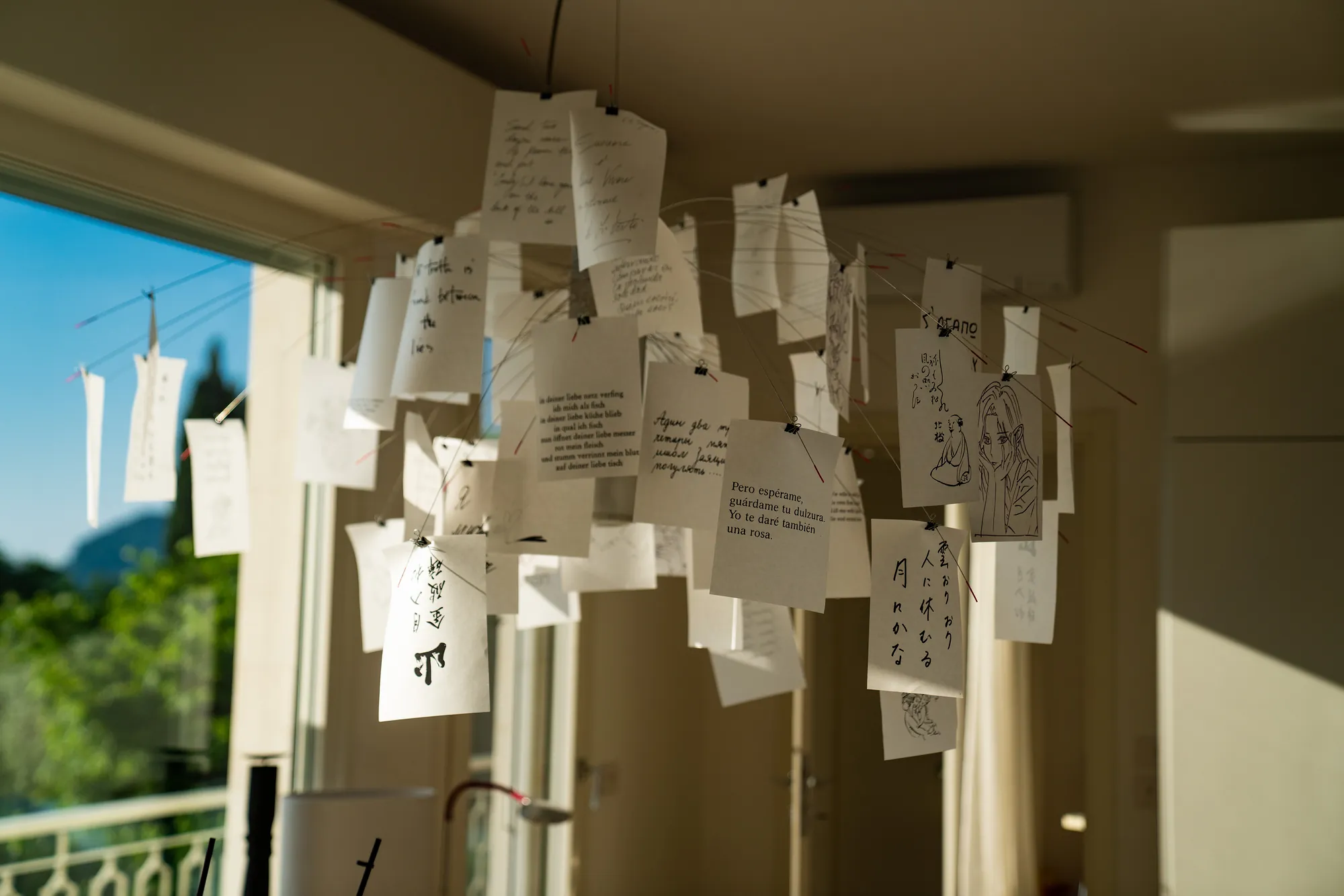 Ingo Maurer Zettel'z chandelier of handwritten paper notes, with the garden beyond the window