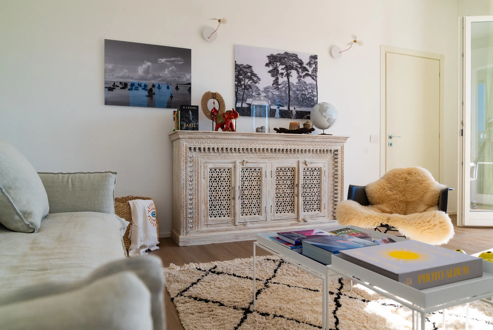 Living area with a carved white sideboard, Berber rug, a chair with sheepskin and photographs on the wall