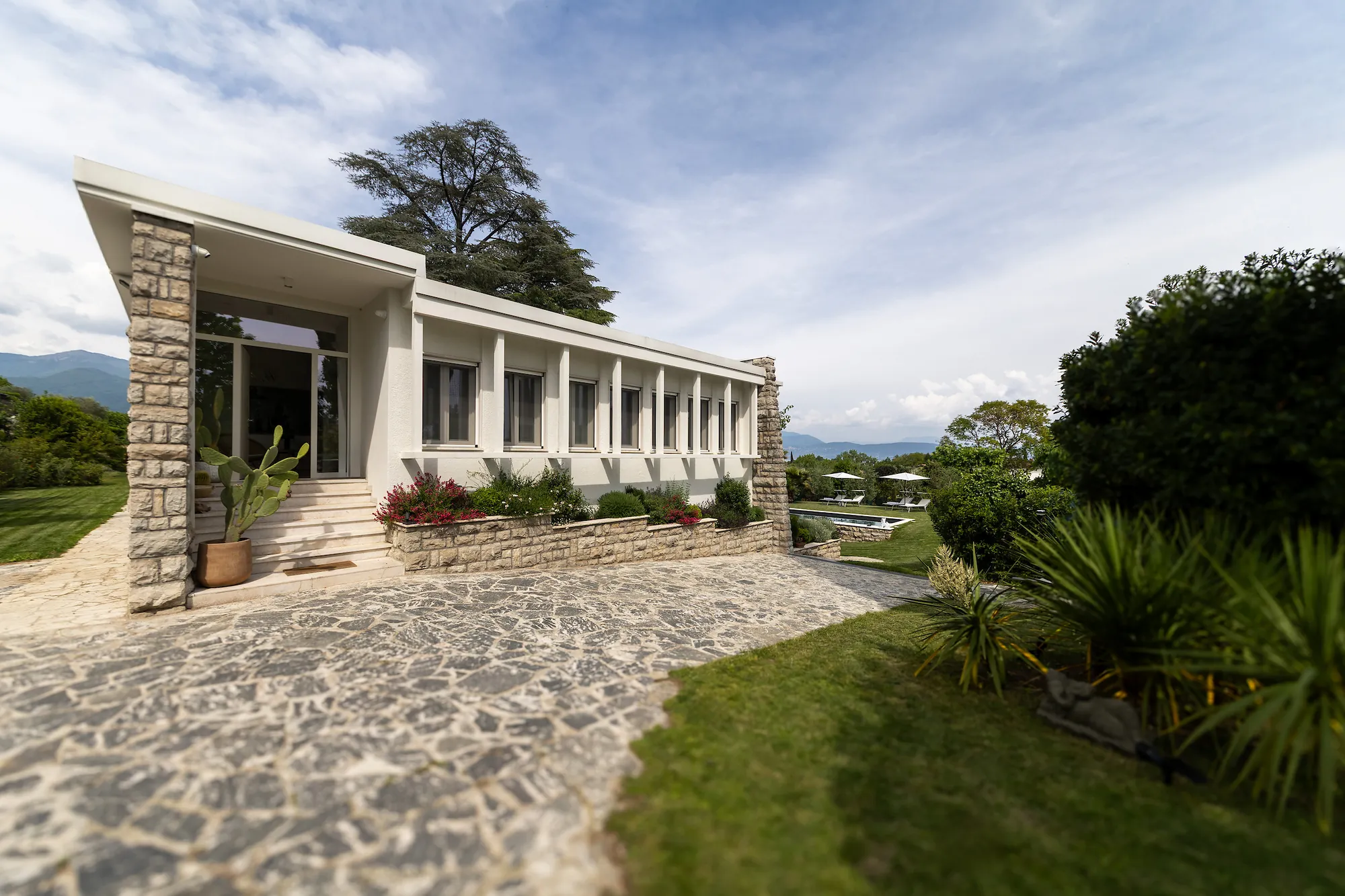 The long white entrance facade of the 1960s architect villa with its stone wall and Mediterranean garden