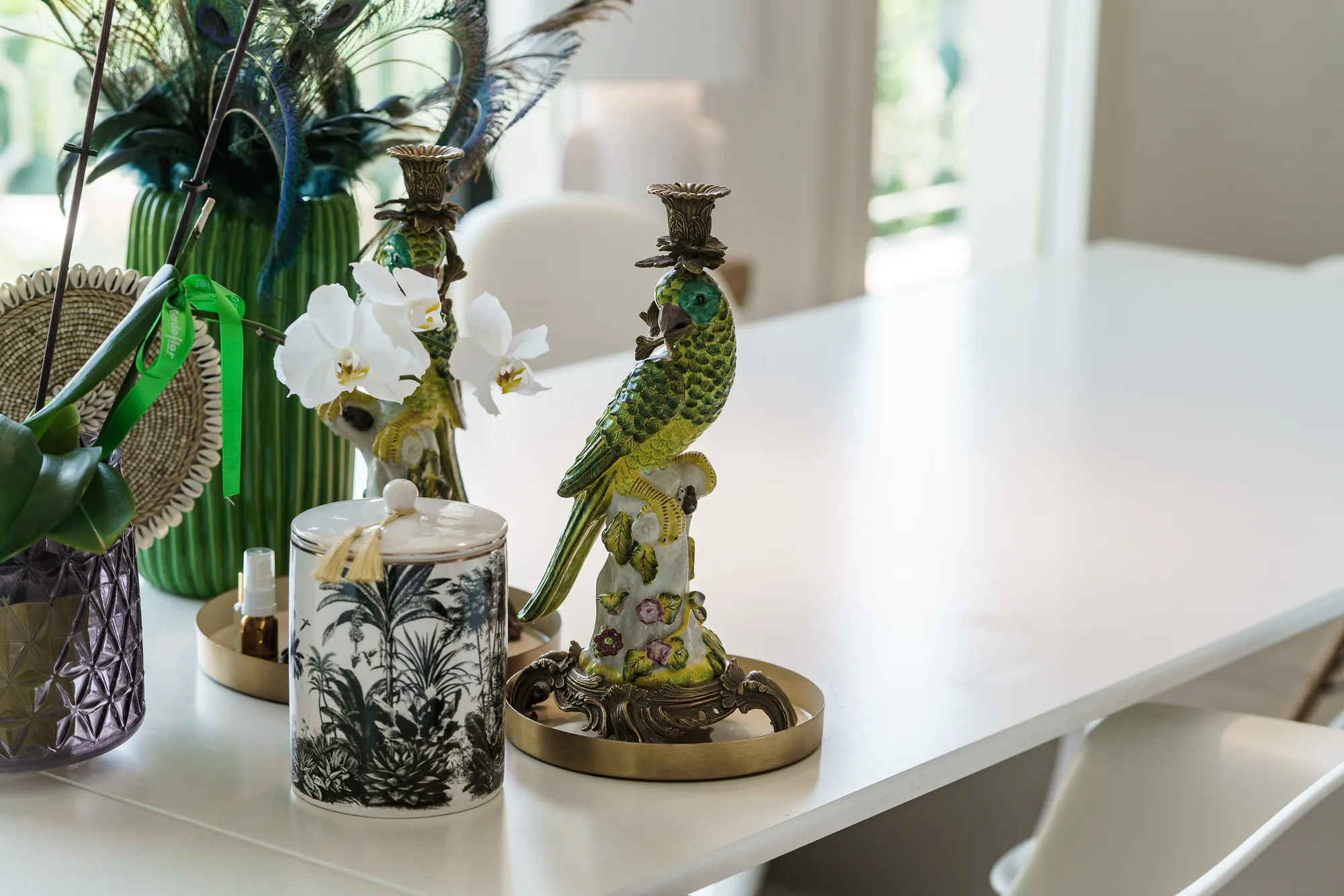 Porcelain parrot candlesticks, an orchid and a printed candle on a white table